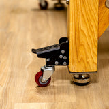 Workbench caster wheel with foot pedal attached to wooden leg on hardwood floor, woodworking tool accessory
