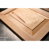 Unfinished wooden cabinet door with beveled raised panel on workshop table