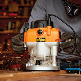 Woodworker using an electric plunge router on wood, producing sawdust in workshop