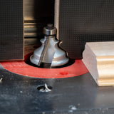 Close-up of a router table with roundover router bit cutting molding profile on wood piece