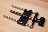 A black and silver metal clamp tool with a threaded screw rod and a black handle, photographed on a light wood surface.