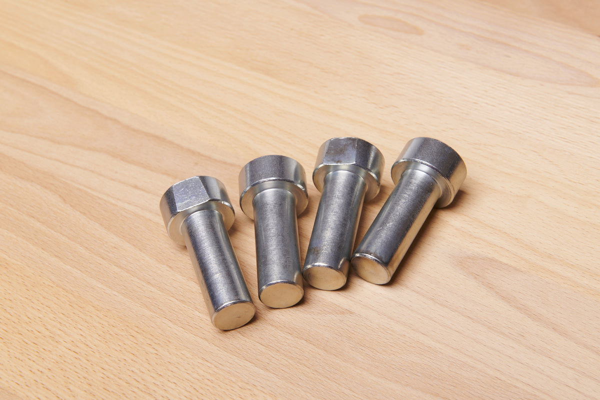 Four silver metal cylindrical pins with hexagonal heads, arranged on a light wood grain surface.