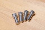 Four silver metal cylindrical pins with hexagonal heads, arranged on a light wood grain surface.