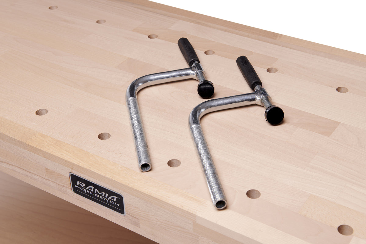 Two dog hole clamps laying on a wood Ramia workbench.