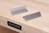Two metal jaw covers sitting on top of a wooden Ramia workbench with Ramia logo displayed on front.