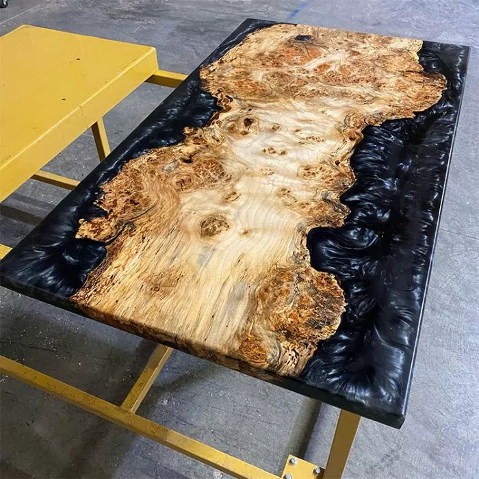 Epoxy resin river table with natural wood slab and black resin on metal legs in workshop