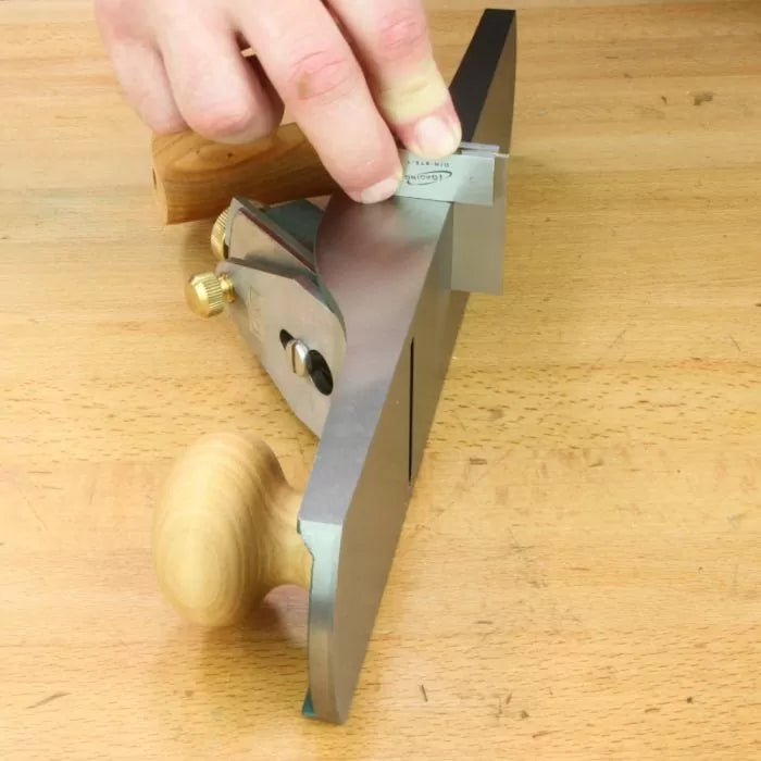 Woodworker checking bench plane flat sole alignment on wooden workbench