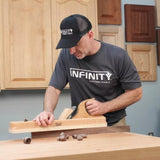 Woodworker using a hand plane on a workbench, wearing a mesh cap in a workshop