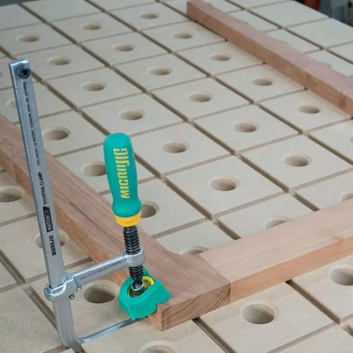 Woodworking clamp securing boards on a perforated workbench for precise assembly