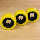 Three yellow woodworking feeder wheels with black centers on a wooden surface