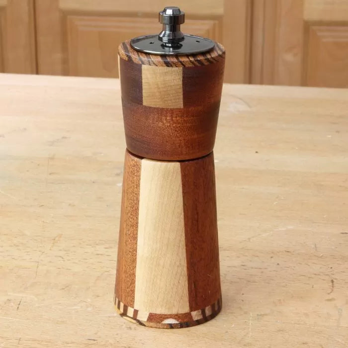 Handcrafted wooden pepper mill with segmented design on a woodworking bench