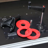 Router table plate with red insert rings, black handle, and adjustment tool for woodworking.
