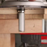 Straight router bit attached to a router cutting through a wood board in a workshop setting.