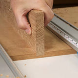 Hand holding a wood board next to a router table fence and measuring guide for woodworking